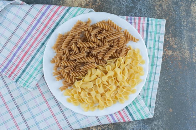 Foto gratuita pasta fusilli marrón y pastas farfalle en el cuenco sobre la toalla, sobre el fondo de mármol.