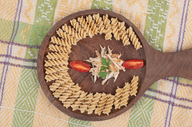 Pasta fusilli y rodajas de pollo sobre tabla de madera.