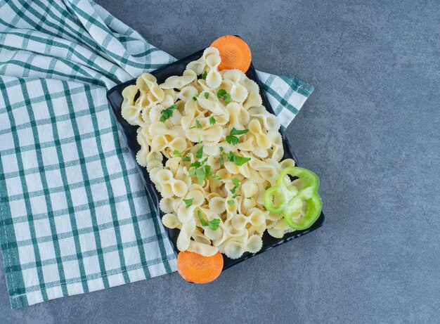 Pasta hervida con verduras en un plato negro.