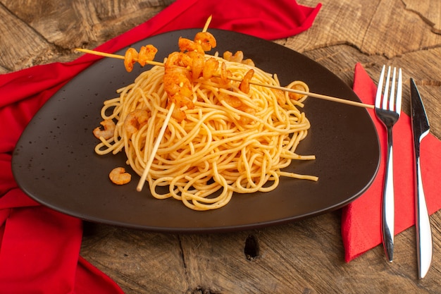 Pasta italiana cocida con camarones dentro de placa marrón con cubiertos sobre madera