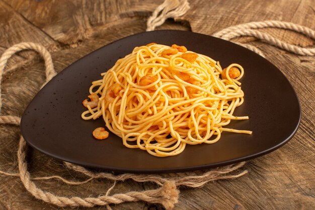 Pasta italiana cocida con camarones dentro de placa marrón con cuerdas en un mostrador de madera