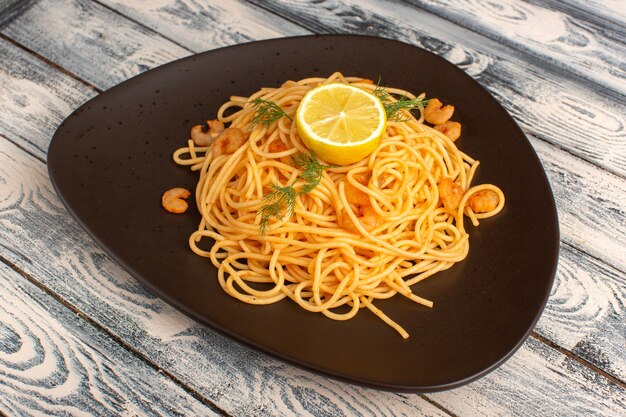 Pasta italiana cocida con camarones verdes y limón dentro de la placa marrón sobre gris