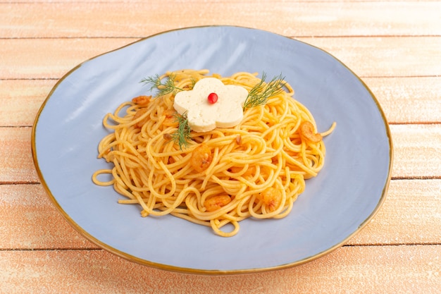 Pasta italiana cocida sabrosa comida con verduras dentro de la placa azul sobre madera crema