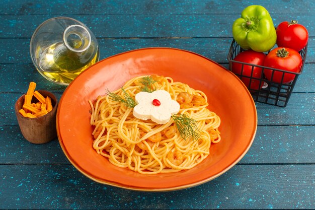 Pasta italiana cocida sabrosa comida con verduras dentro de la placa naranja sobre madera azul