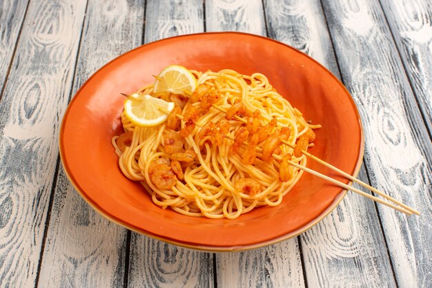 Pasta italiana cocida sabrosa con rodajas de limón y camarones dentro de la placa naranja sobre gris