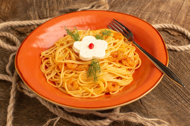 Pasta italiana cocida con verduras dentro de placa naranja sobre madera