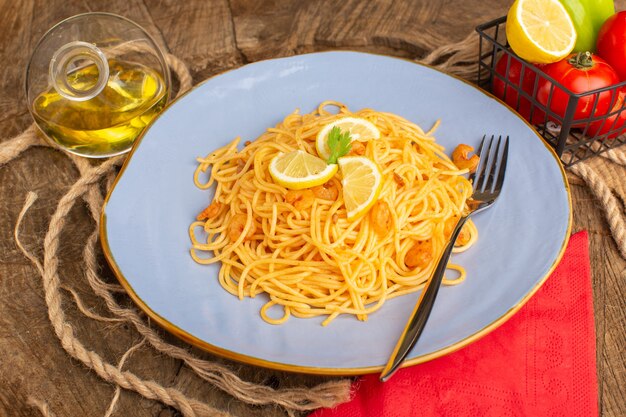 Pasta italiana cocida con verduras y rodajas de limón junto con verduras y aceite dentro de azul