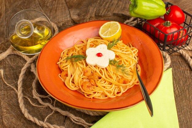 Pasta italiana cocida con verduras y rodajas de limón junto con verduras y aceite dentro de la placa de naranja sobre madera