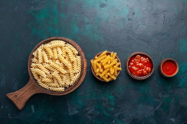 Pasta italiana en forma de vista superior con salsa y condimentos en el escritorio azul oscuro