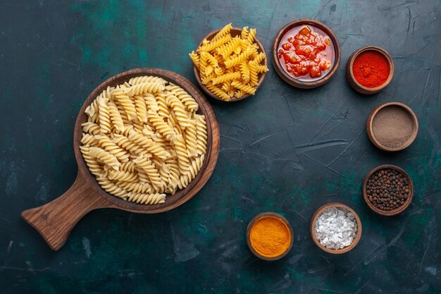 Pasta italiana en forma de vista superior con salsa y diferentes condimentos en el escritorio azul oscuro