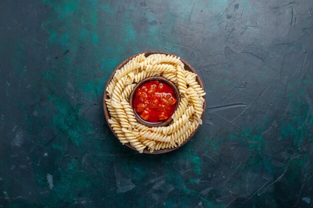 Pasta italiana en forma de vista superior con salsa de tomate en el escritorio azul oscuro