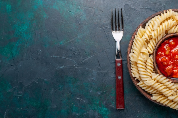 Pasta italiana en forma de vista superior con salsa de tomate y tenedor sobre fondo azul oscuro