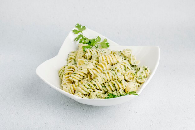 Pasta italiana con hierbas verdes en un tazón blanco.