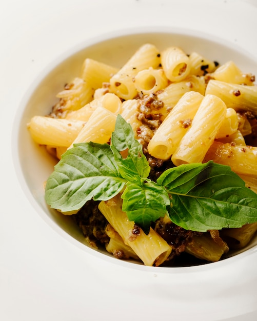 Pasta italiana penne con especias y albahaca dentro de un tazón blanco en fondo blanco.