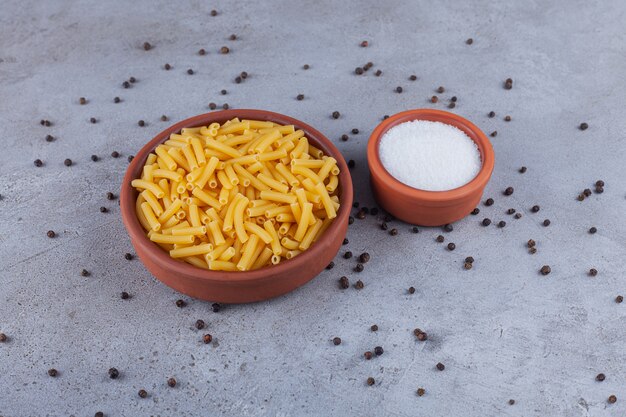 Pasta italiana penne seca en un recipiente redondo con granos de pimienta sobre una mesa de piedra.