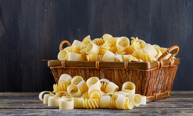 Pasta de macarrones en una cesta sobre un fondo oscuro y de madera. vista lateral.