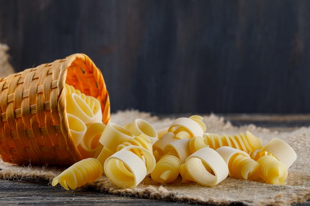 Pasta de macarrones en un pequeño cubo sobre una tela de saco y fondo oscuro. vista lateral. espacio libre para su texto