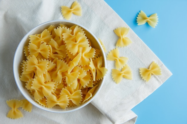 Pasta de macarrones en un recipiente sobre un fondo de tela y azul cian. vista superior.