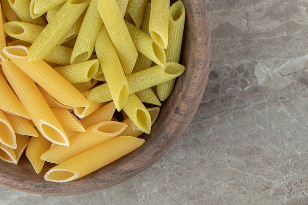 Pasta penne amarilla y verde en un tazón de madera.