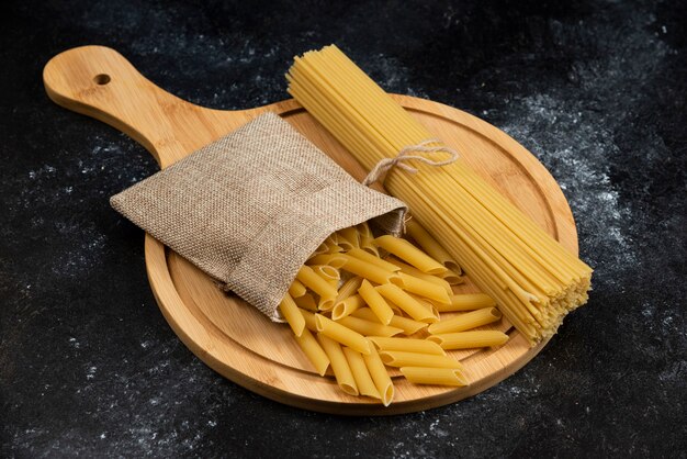 Pasta penne en una cesta rústica con espaguetis en una bandeja de madera.