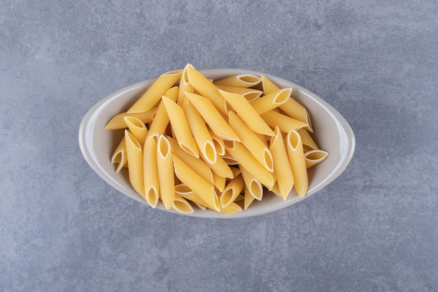 Pasta penne cruda en cuenco de cerámica.