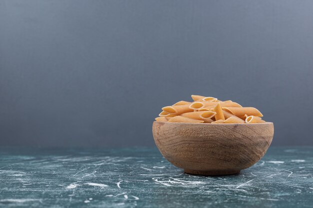 Pasta penne cruda marrón en un tazón de madera. Foto de alta calidad