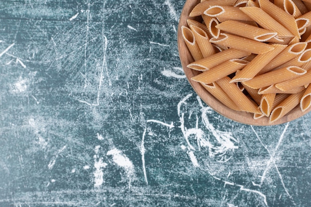 Pasta penne cruda marrón en un tazón de madera. Foto de alta calidad