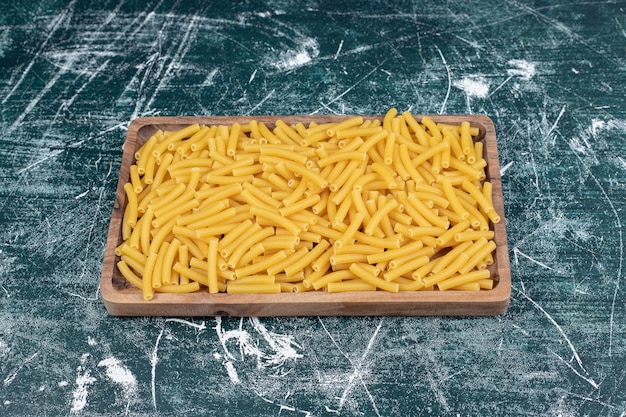 Pasta penne cruda en placa de madera. Foto de alta calidad