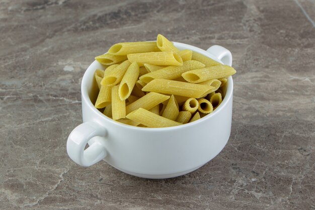 Pasta penne cruda en taza blanca