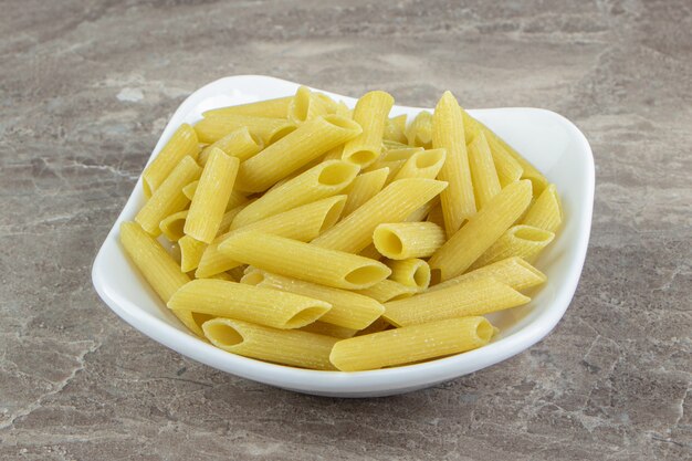 Pasta penne cruda en tazón de fuente blanco