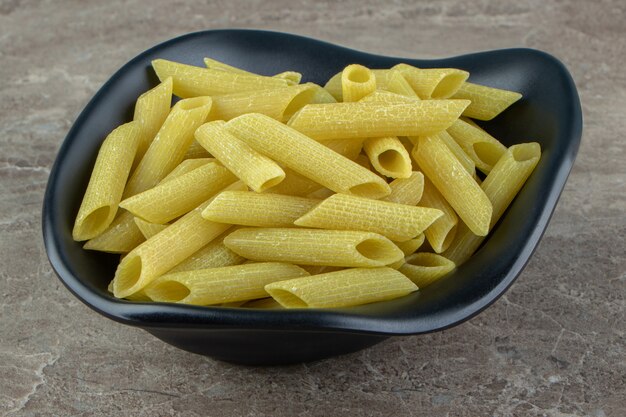 Pasta penne cruda en un tazón negro.