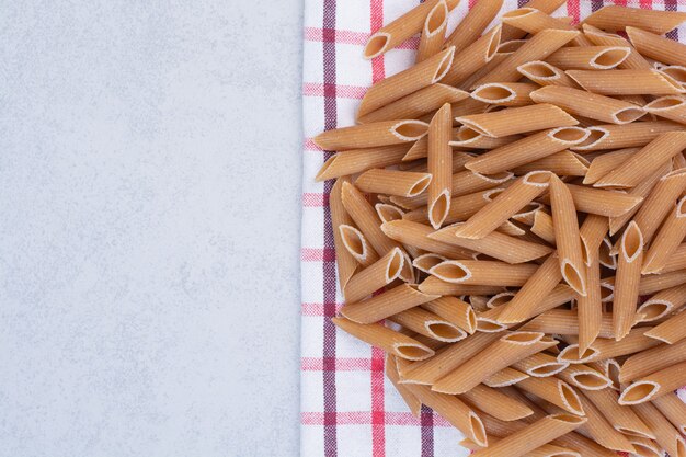 Pasta penne marrón cruda sobre mantel rayado