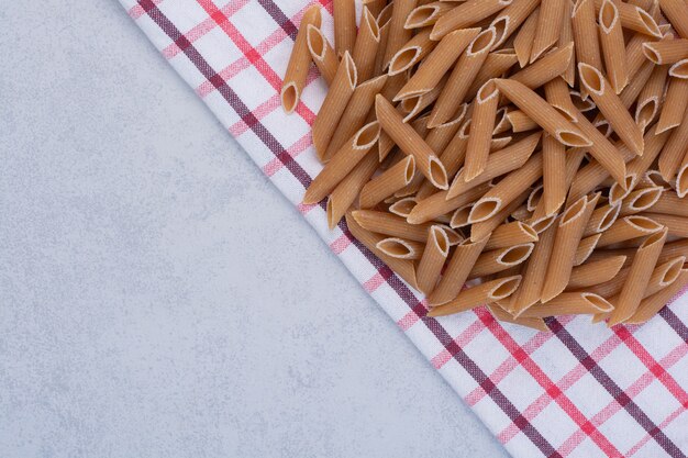 Pasta penne marrón cruda sobre mantel rayado