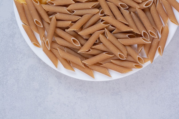 Pasta penne marrón sobre placa blanca.