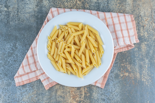 Pasta penne en el plato, en la toalla, en la superficie de mármol.