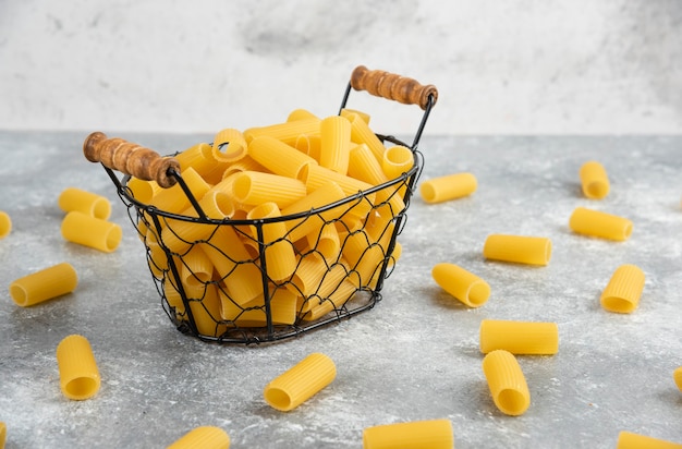 Pasta penne en un recipiente metálico sobre mesa de mármol gris.