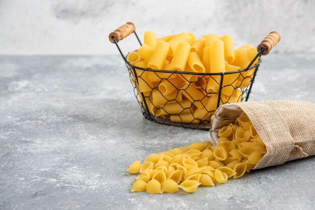 Pasta penne en un recipiente metálico sobre mesa de mármol gris.