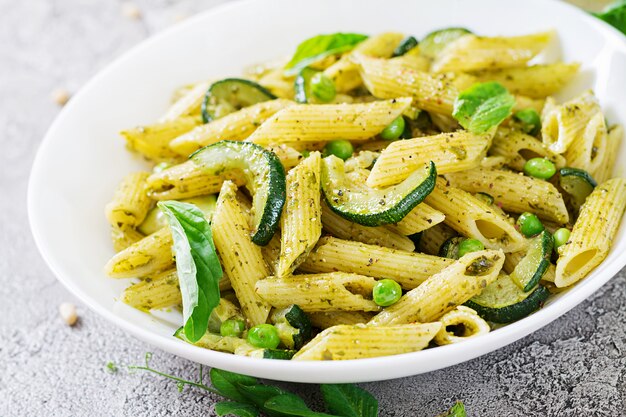 Pasta penne con salsa de pesto, calabacín, guisantes y albahaca. Comida italiana.