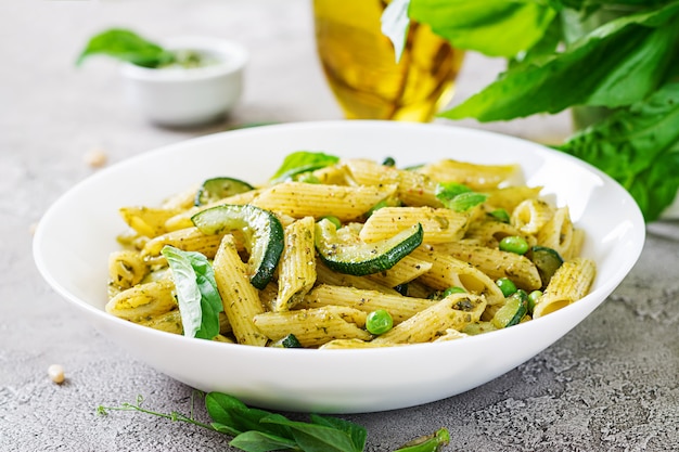 Pasta penne con salsa de pesto, calabacín, guisantes y albahaca. Comida italiana.