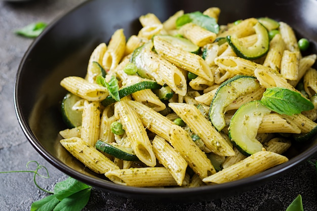 Pasta penne con salsa de pesto, calabacín, guisantes y albahaca. Comida italiana.