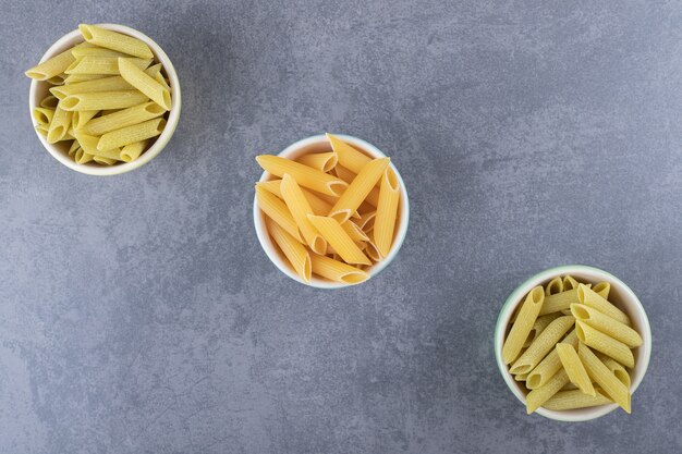 Pasta penne verde y amarilla cruda en tazones de colores.