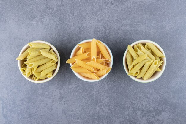 Pasta penne verde y amarilla cruda en tazones de colores.