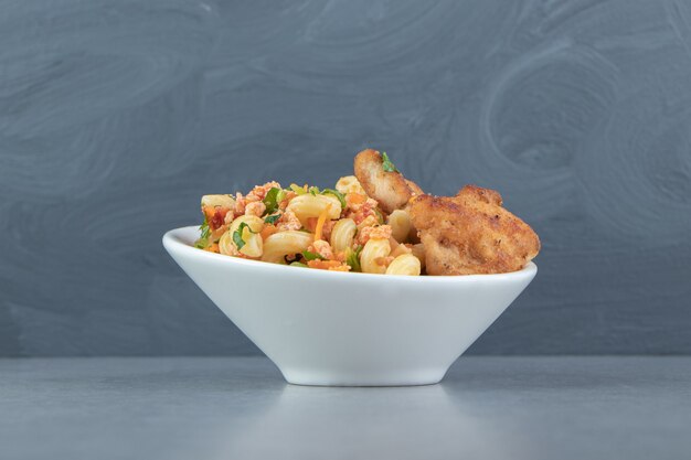 Pasta con pollo frito en tazón de fuente blanco.