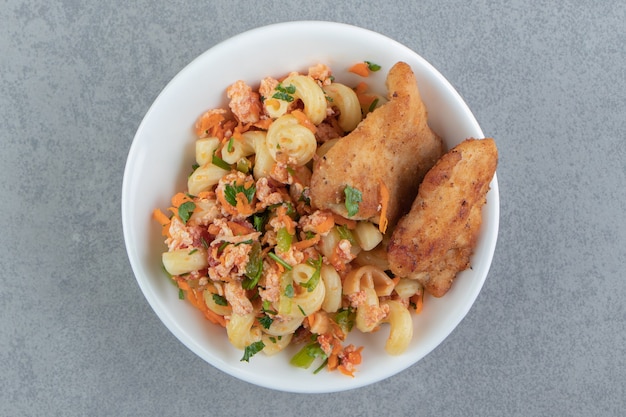 Pasta con pollo frito en tazón de fuente blanco.