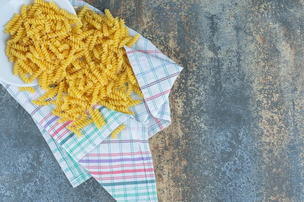 Pasta que cae del cuenco volcado, sobre el fondo de mármol.