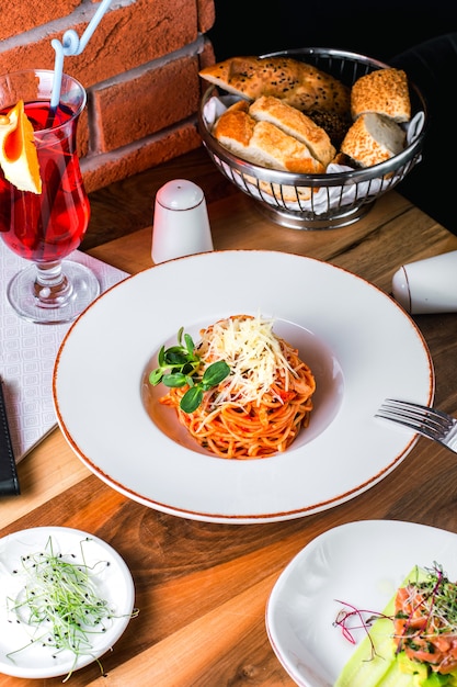 Foto gratuita pasta con queso rallado y albahaca servida con cóctel y pan