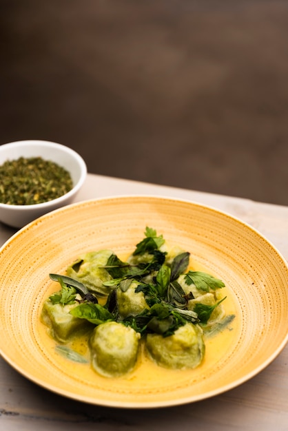 Foto gratuita pasta de ravioles verdes servida en plato con tazón de hierbas