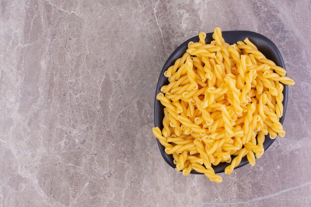 Pasta en un recipiente de cerámica negra aislado sobre superficie gris