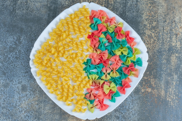 Foto gratuita pasta rizada con pastas de pajarita en un plato, sobre la superficie de mármol.