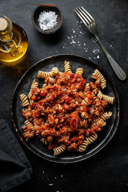 Pasta con salsa boloñesa servida en plato sobre fondo oscuro